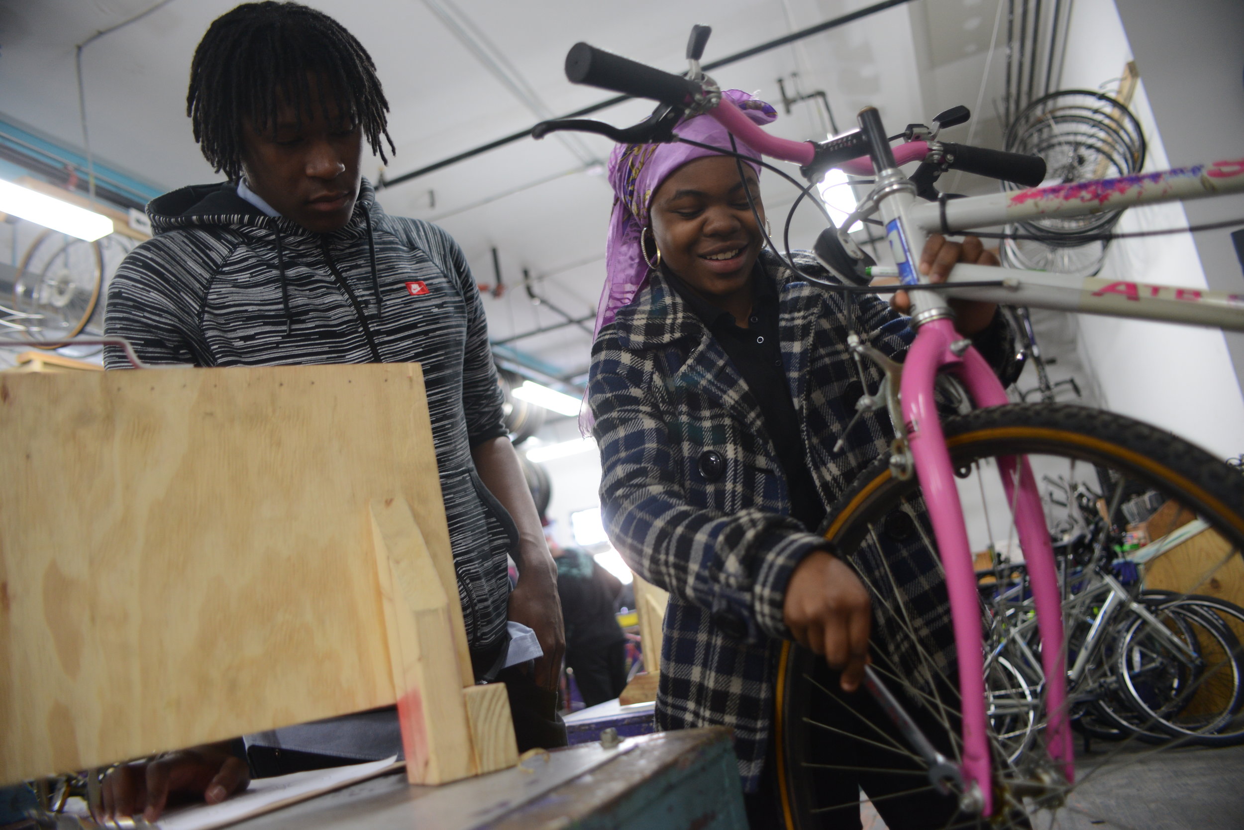 Two people smiling, working on a bike at a bike shop