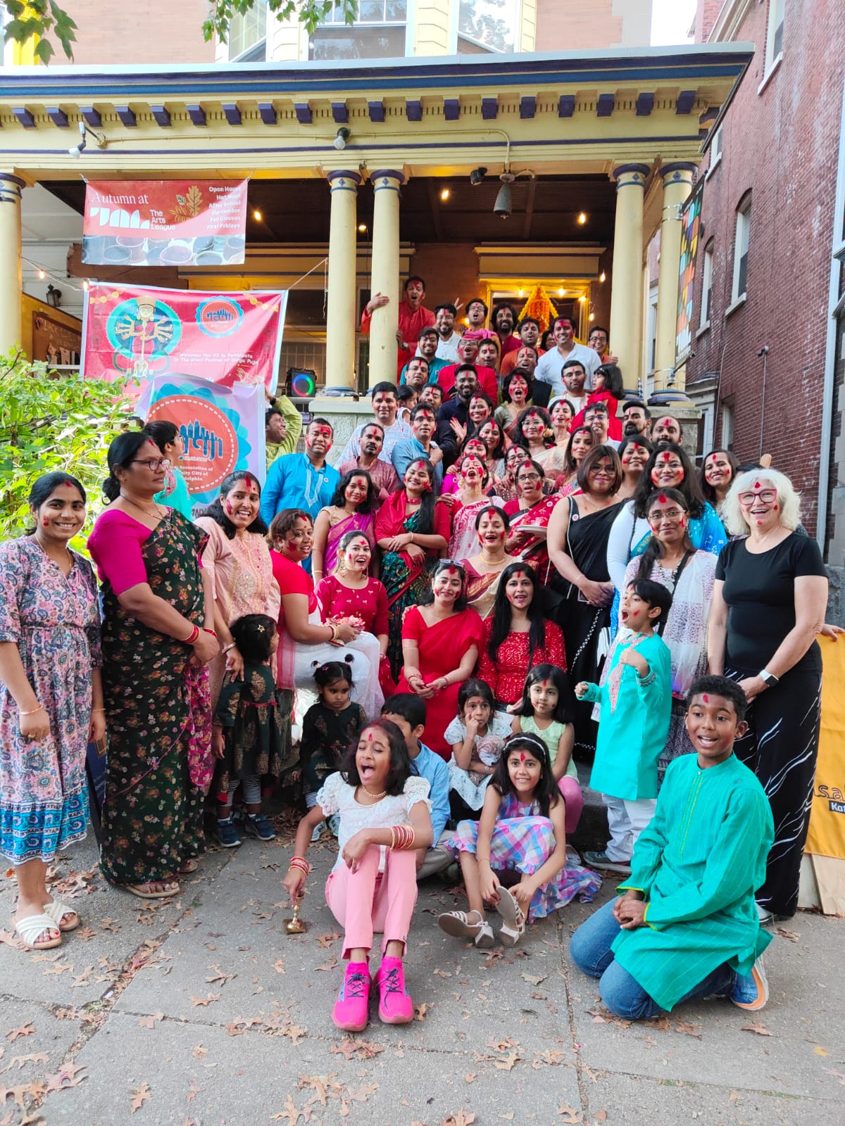 People sitting on the front step of a row home smiling. Many of the people wear traditional clothing and are celebrating the annual Bengali Cultural Celebation