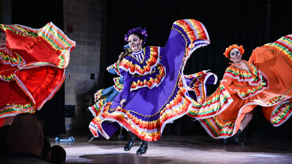 Women dancing while wearing cultural dresses for Dia De los Muertos