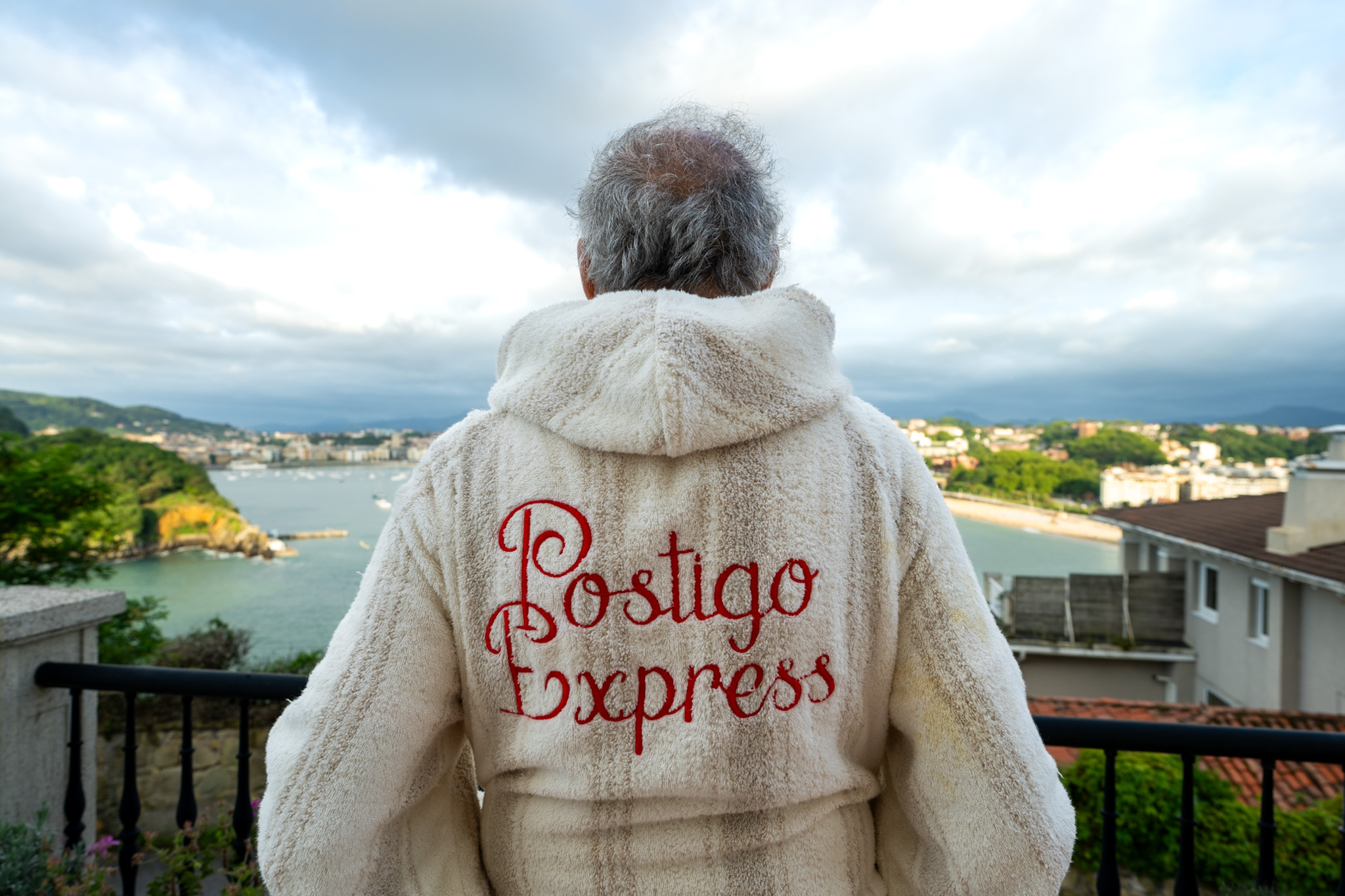 A man stands with his back to the camera. the back of his furry white robe reads “Pestigo Express” in red letters
