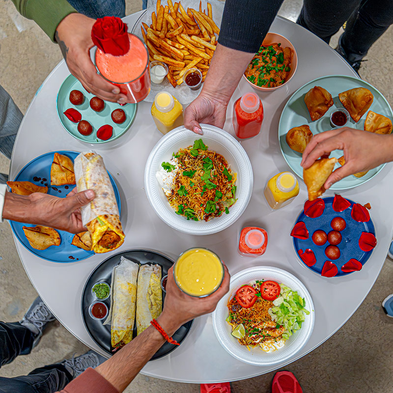 Aerial view of a table at Bowl'd Masala. People share wraps, samosa, and smoothies across the table.