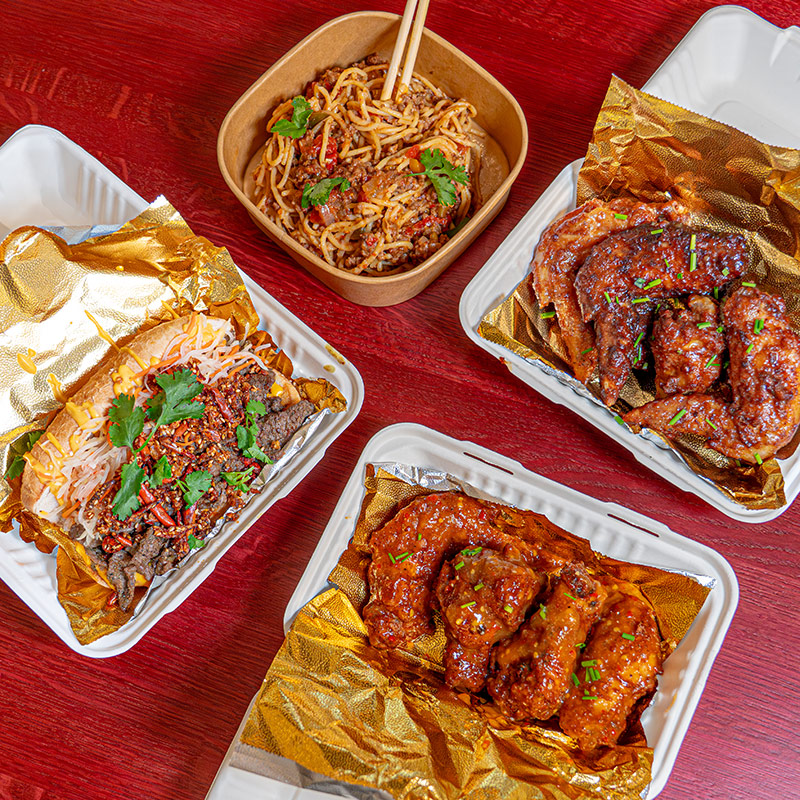 Plates of food from Sahhby, featuring wings, noodles, and a lemongrass cheesesteak
