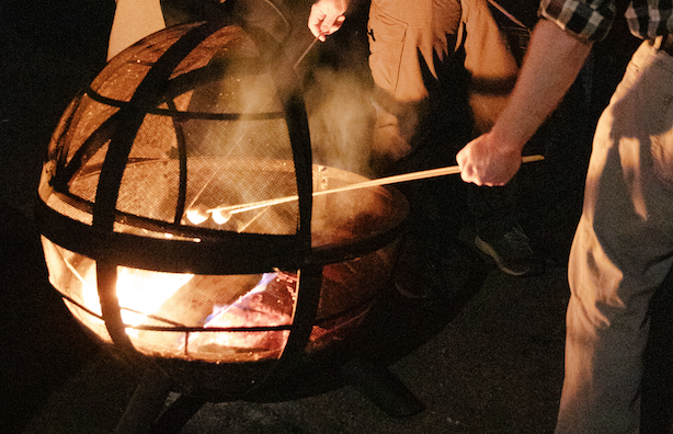 A group of people roast marshmallows over a firepit