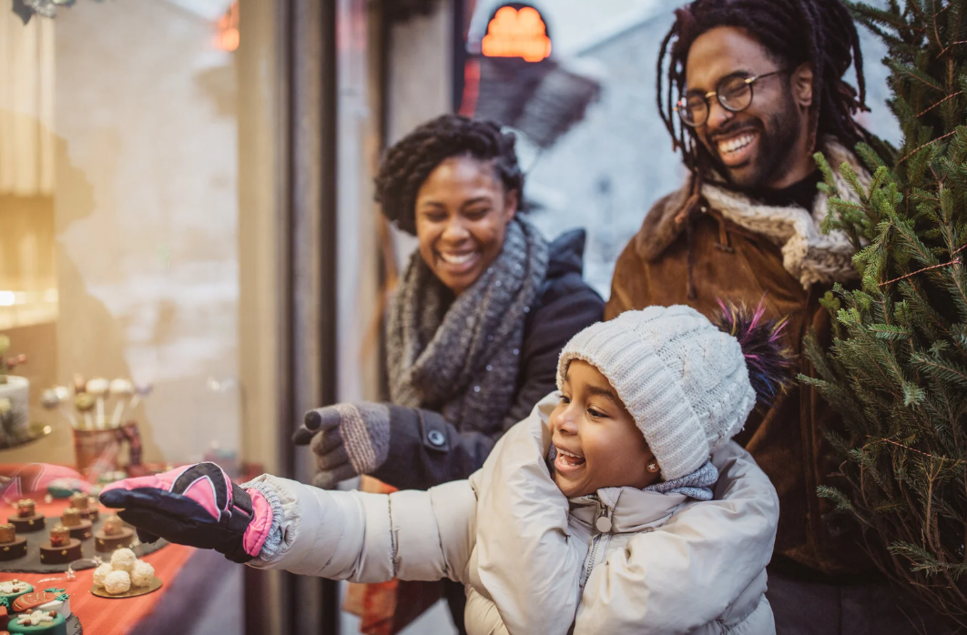 Young family on Christmas market. They walking around and picking what to buy. Holding gift boxes and Christmas tree