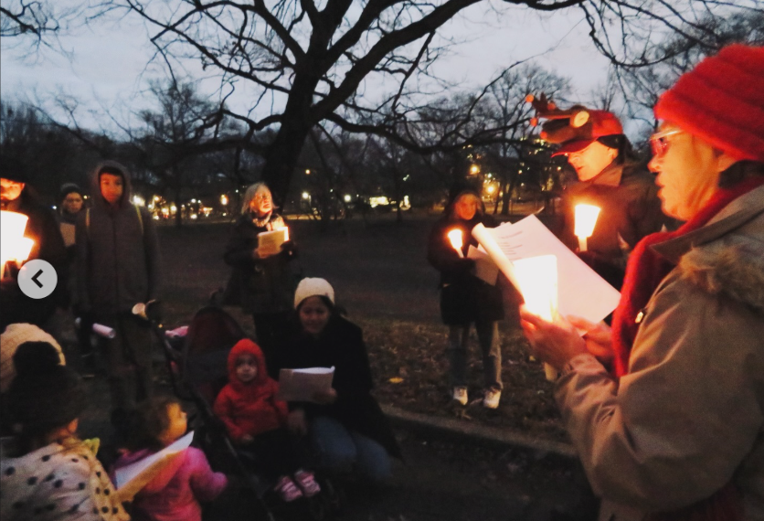 A group of people singing Christmas Carols at dusk in Clark Park