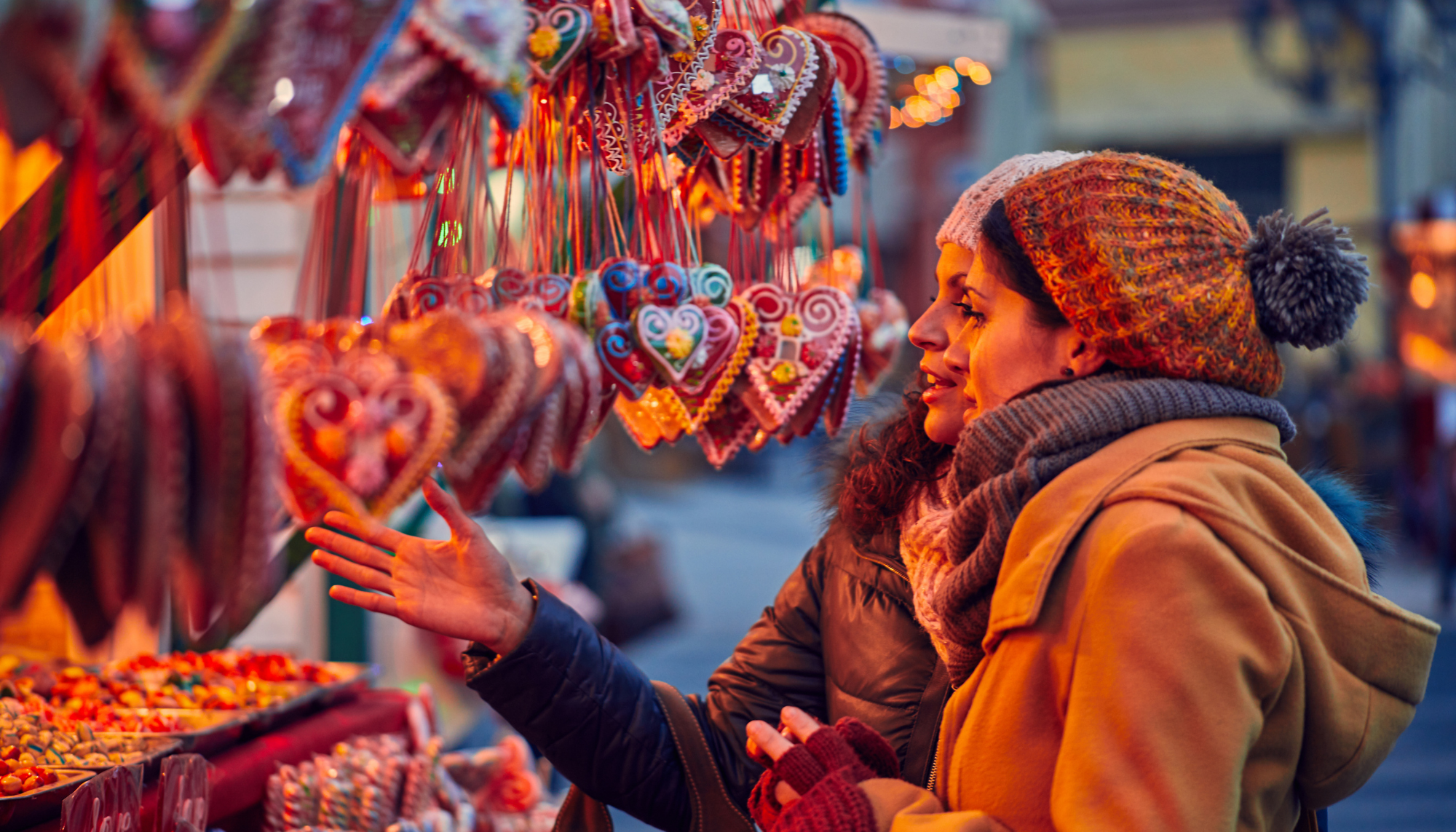 Two women shop at a christmas market. they are bundled up in jackets, hats and scarves