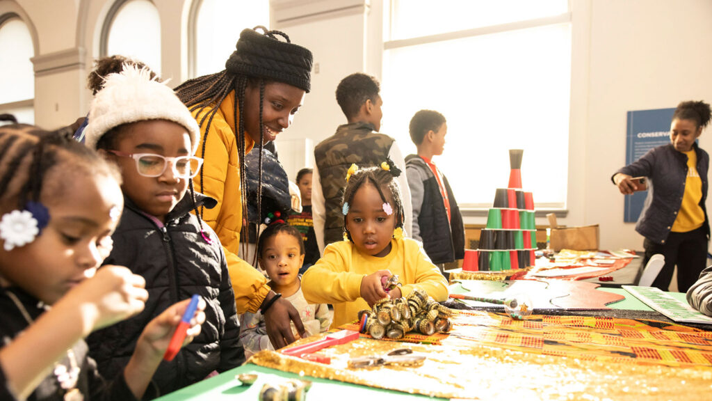 A chaperone engages with a group of children participating in a Kwanza craft event.