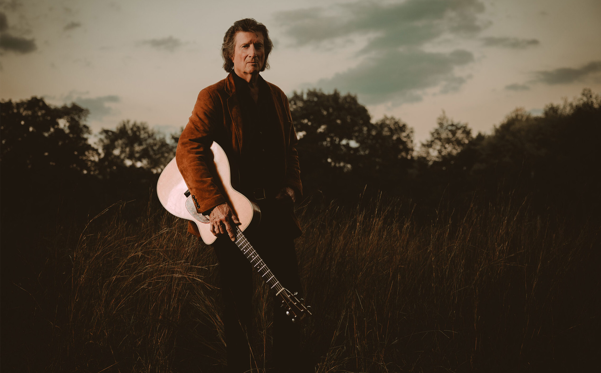 A promotional image of singer Loudon Wainwright III & Chris Smither standing in a field, holding a guitar