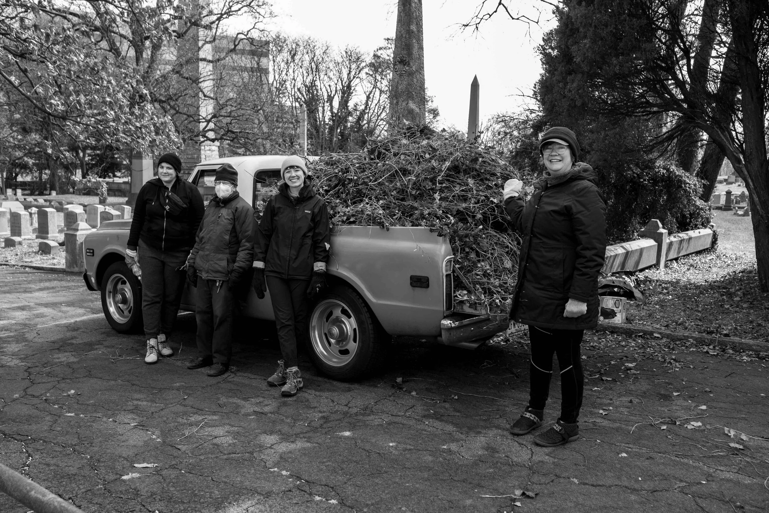 Volunteers sanding in front of a truck full of sticks, trees, and trash they collected during a volunteer day at the Woodlands Cemetery