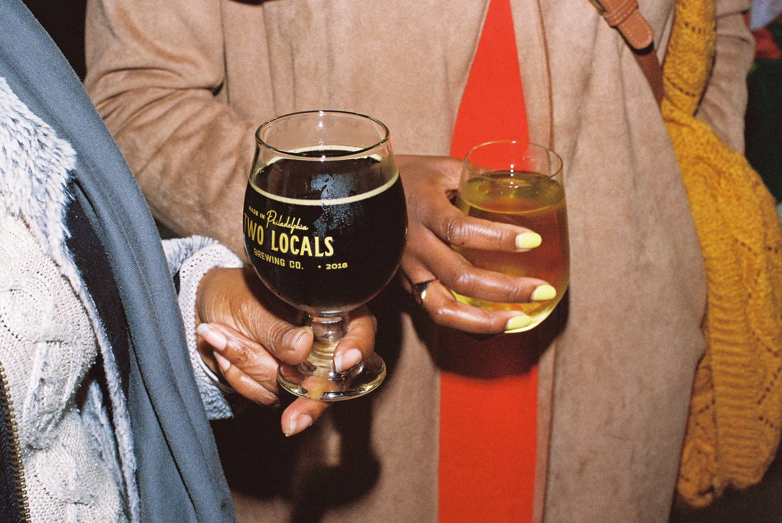 People hold beer in glasses branded with Two Locals' logo