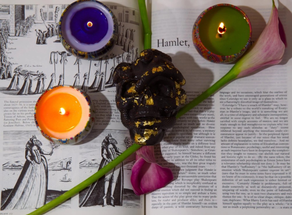 An image of a skull, candles, and a flower over the script from the play Hamlet