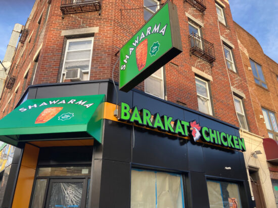 Top of building is brick, lower part of the building is black with three signs that say BARAKAT CHICKEN on green backgrounds with illustrations of a chicken and shawarma.