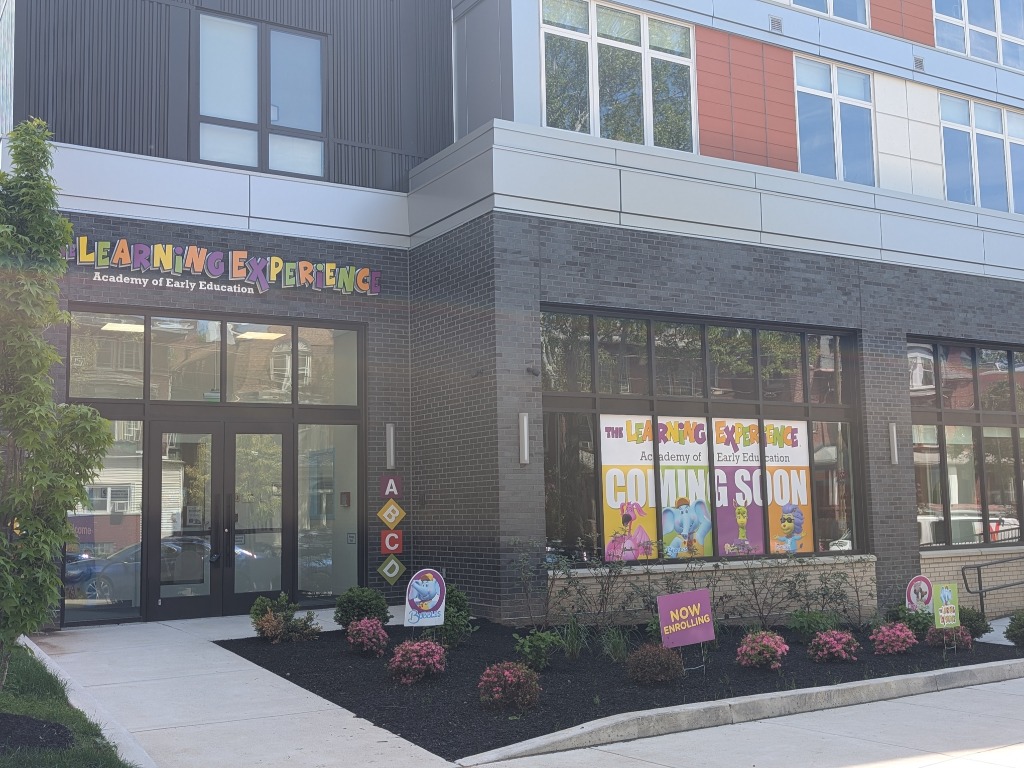 A black, grey, and red building says THE LEARNING CENTER in different rainbow colors. The building has a front garden and paved walkway.