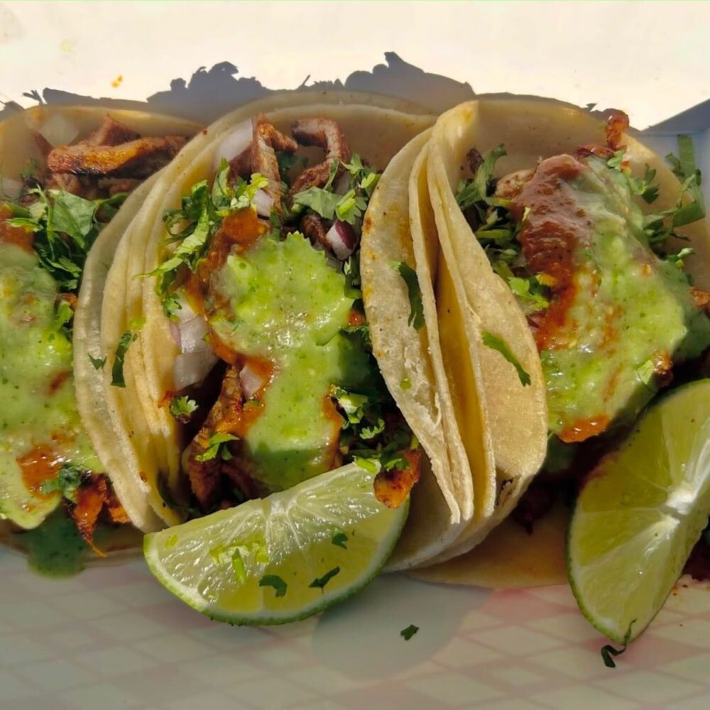 Three tacos with green sauce and lime